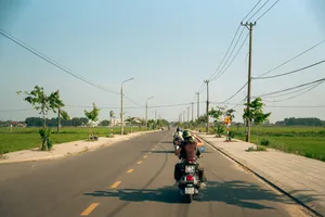 Jalan pedesaan Hoi An dalam tur Vespa, pengendara melaju di jalur kecil di antara sawah dan tiang listrik pinggir jalan