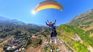 Tandem paraglider soaring above terraced rice fields and mountain valleys with Sapa Paragliding under a bright canopy over Sapa