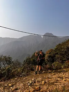 Hiker stands on a rocky ridge trail in Sapa, raising a hand while trekking through sunlit mountain mist