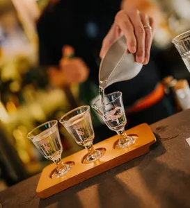Pouring sake into small tasting glasses from a bottle at a rare Singapore session, with three glasses on a wooden tray
