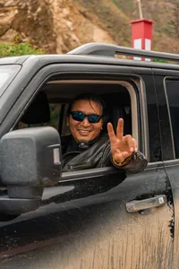 Tibetan guide smiling and making a peace sign from a jeep window on the road during the 6-day Shangri-La Loop