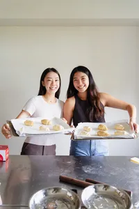 Two learners hold trays of shio pan rolls, with mixing bowls and a rolling pin on the table during workshops in Singapore
