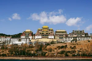 Traditional white-and-red temple complex with gilded rooftops above a riverbank in Shangri-La under a wide blue sky