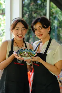Two Indigenous Sabahan women in aprons holding a colourful bowl of salad during a local cooking experience in Kota Kinabalu, Sabah