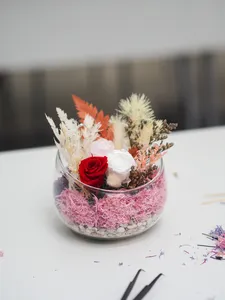 Preserved floral bowl terrarium with a red rose and orange blooms on pink moss, surrounded by petals on a worktable in Singapore