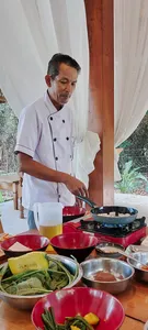 Chef Michael stirs on a skillet beside red bowls and plates during a Traditional Manggarai vegan cooking class in Labuan Bajo