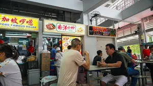 Singapore hawker centre tables where diners chat and eat by a busy stall counter beneath rojak menu signs — Singapore hidden gems