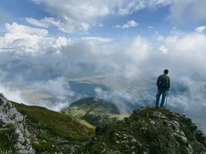Hiker with trekking poles standing on a rocky ridge as mist and clouds drift over valleys during the Jade Dragon hike
