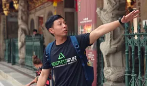 Triad Trails guide gestures as he leads a walking tour in Singapore, speaking to visitors beside old buildings