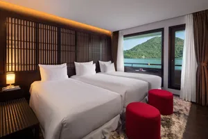 Oasis Bay Party Cruiser cabin with twin beds, red stools and curtains, with karst islands and bay water visible on the Halong Bay