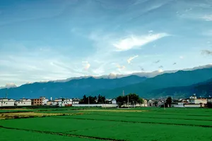 Sawah hijau, bangunan halaman putih, dan pergunungan di kejauhan di bawah langit biru di Dali, Yunnan
