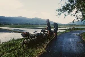 Cyclists pause beside rural fields in Langkawi on Bicycle Day Langkawi, with bikes by the water and distant hills