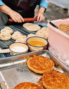 Round dough breads cook on a griddle as a cook flips them, with trays of seasoning and sauce on a Lijiang street-food table