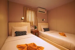 Two single beds in a cosy Seaventures Dive Rig cabin, with orange towel wraps, an air conditioner and warm light