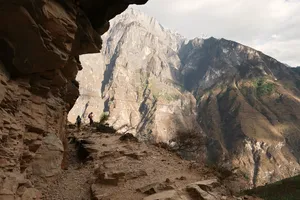 Hikers on the High Trail of Tiger Leaping Gorge in Lijiang, framed by steep rock walls and mountain valley views