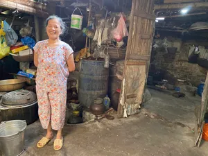 Smiling woman standing in a rustic kitchen with cooking pots during a traditional tofu-making visit in Hanoi’s Red River village