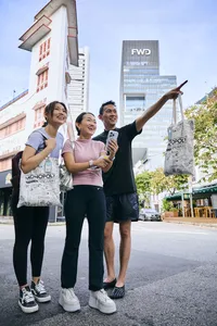一群人在新加坡河畔的街头参与现实版大富翁游戏,摆姿势合影并手拿托特包——新加坡小众宝藏体验
