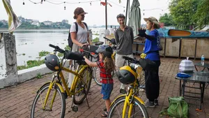 Travellers on yellow bikes pause by the riverside on a Mekong Island trip from Ho Chi Minh City, with a boat behind