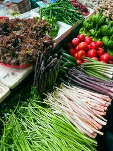 Lijiang market stall piled with seasonal greens, chillies and tomatoes for a Yunnan cooking day, ready for the morning market walk