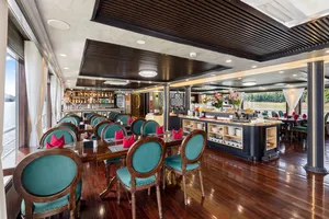 Bar lounge on the Oasis Bay Party Cruiser with teal upholstered chairs and a central drink counter for socialising in Halong Bay