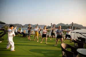 Guests performing a group stretch on a luxury cruise deck with sea views and limestone scenery in Halong Bay