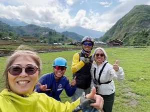 Group of paragliding passengers in helmets smiling and giving thumbs up on a grassy launch field in the hills, Sapa