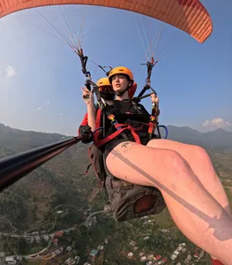 Tandem paragliding close-up of an orange-helmeted passenger reclining in the harness as the pilot glides over valley farmland in Sapa