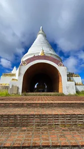 White stupa doorway under dramatic clouds with gold details beside a brick courtyard in Khao Sok National Park