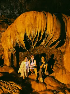 Three travellers posing in a cave under a glowing yellow rock formation during a Cao Bang motorbike journey