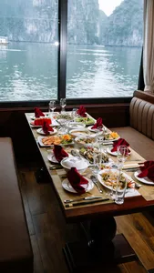 Dining table set with seafood dishes in a Cat Ba cruise cabin, framed by tall windows overlooking misty bay water