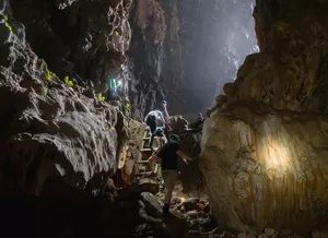 Phong Nha Cave day trip with Moc Nam Adventure: travellers walk through a dark limestone grotto lit by headlamps