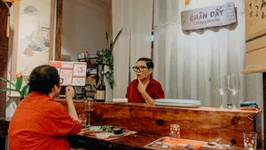 Host in a red robe welcomes guests at Chan Dat Living Room in Hoi An, with wine glasses and tasting materials on the table