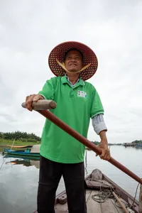 今天在会安,一位穿着绿色上衣、戴着斗笠的当地船夫在木船上手持船桨微笑