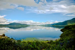 Calm Napa Lake in Shangri-La framed by forested hills and mountains under cloudy skies, with mirror-like reflections