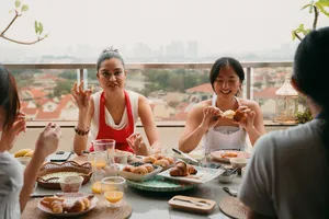 Balcony breakfast in Singapore: people hold freshly baked croissants at a long table with city skyline beyond the railing