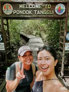 Smiling travellers posing with peace signs by a welcome gate sign for Tanjung Puting National Park, on the boardwalk