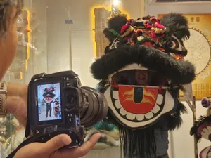 Traditional lion dance performer wearing an ornate headpiece stands while a camera films inside a Ho Chi Minh City cultural heritage room