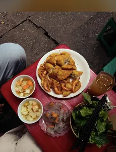 Fried appetisers with fresh herbs and dipping bowls on a red table at a Hanoi street food stop