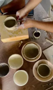 Hands glazing ceramic cups and bowls on a pottery table at Ilham Ceramic Studio in Langkawi’s village workshop