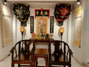 Temple room with two ornate lion dance masks above lanterns, Chinese posters on the walls, and a ceremonial prayer table in Ho Chi Minh City