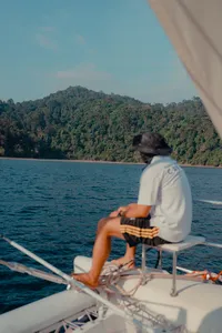 A traveller relaxing on SY Mawali catamaran, watching lush green coastline drift by near Kota Kinabalu
