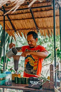 Community stall worker pouring from a large kettle under a palm roof in Khao Lak for a conservation-focused tour