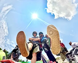 Paragliding team basking in the sun during take-off with multiple riders’ shoes and harnesses visible against blue sky, Sapa