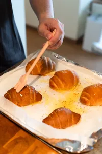 Hand using a brush to glaze shio pan buns on a parchment tray before baking—workshops in Singapore