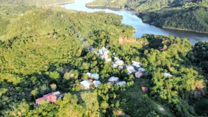 Aerial view of clustered homes, forest, and a winding river at a Bidayuh ancestral land regenerative homestead near Kuching