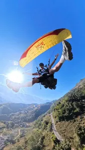 Paraglider rider in mid-air with a yellow canopy framed against bright blue sky and a winding mountain valley road, Sapa