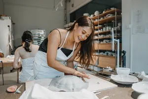 Singapore pottery workshop: instructor shaping a ceramic plate on a workbench with tools, as another participant works in the back