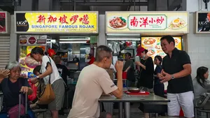 Hawker centre rojak stall in Singapore with cooks preparing food behind the counter as diners wait under menu boards — Singapore hidden gems