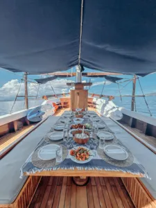 Dinner table laid out on a deluxe phinisi deck with served dishes and cutlery at sea during a cruise to Komodo Island