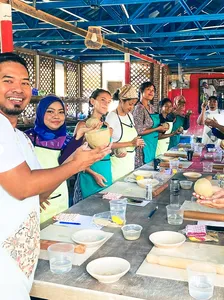 Group pottery class at Ilham Ceramic Studio in Langkawi with participants glazing clay bowls on a shared worktable
